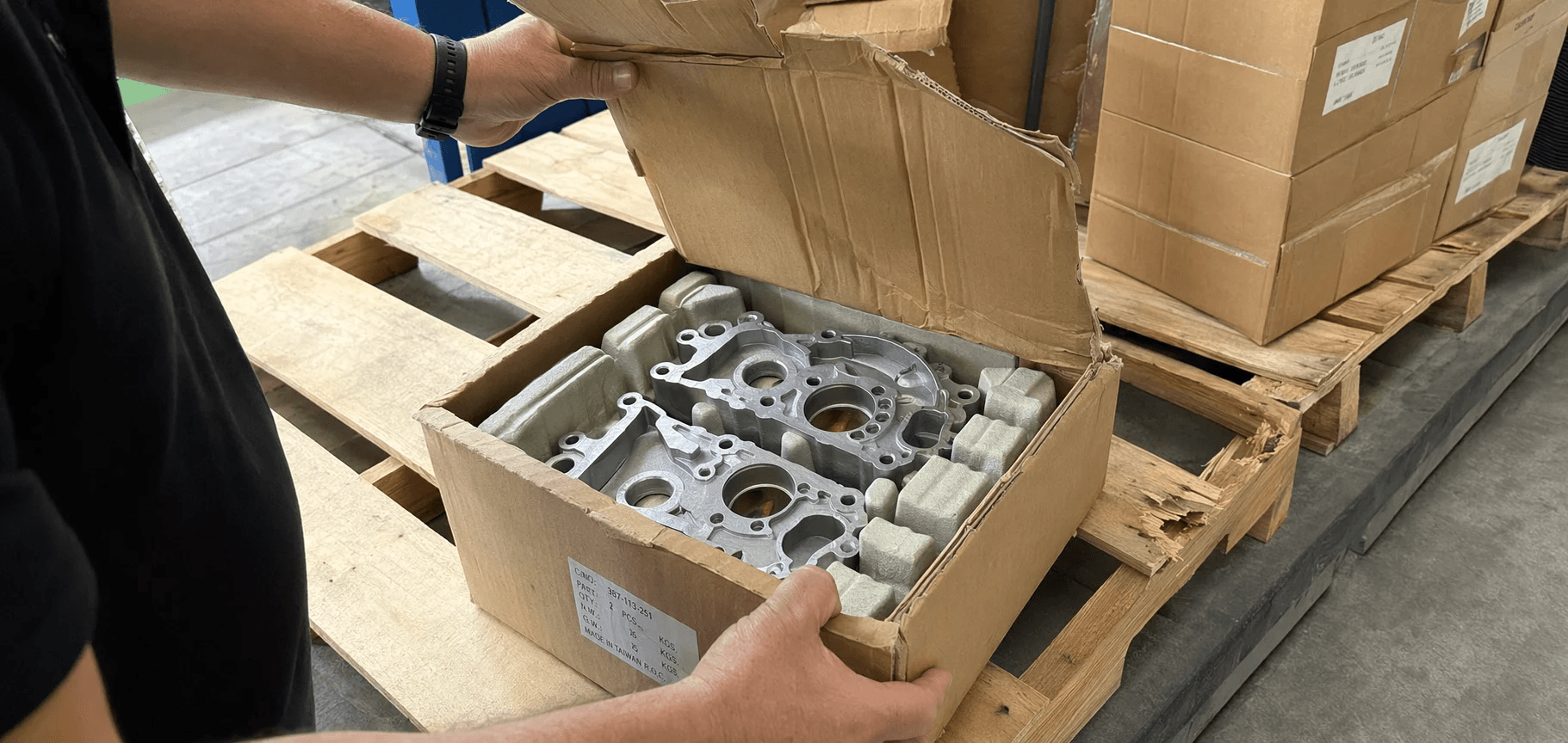 An engineer inspecting three air-freighted pallets of die-cast parts with different levels of packaging damage.